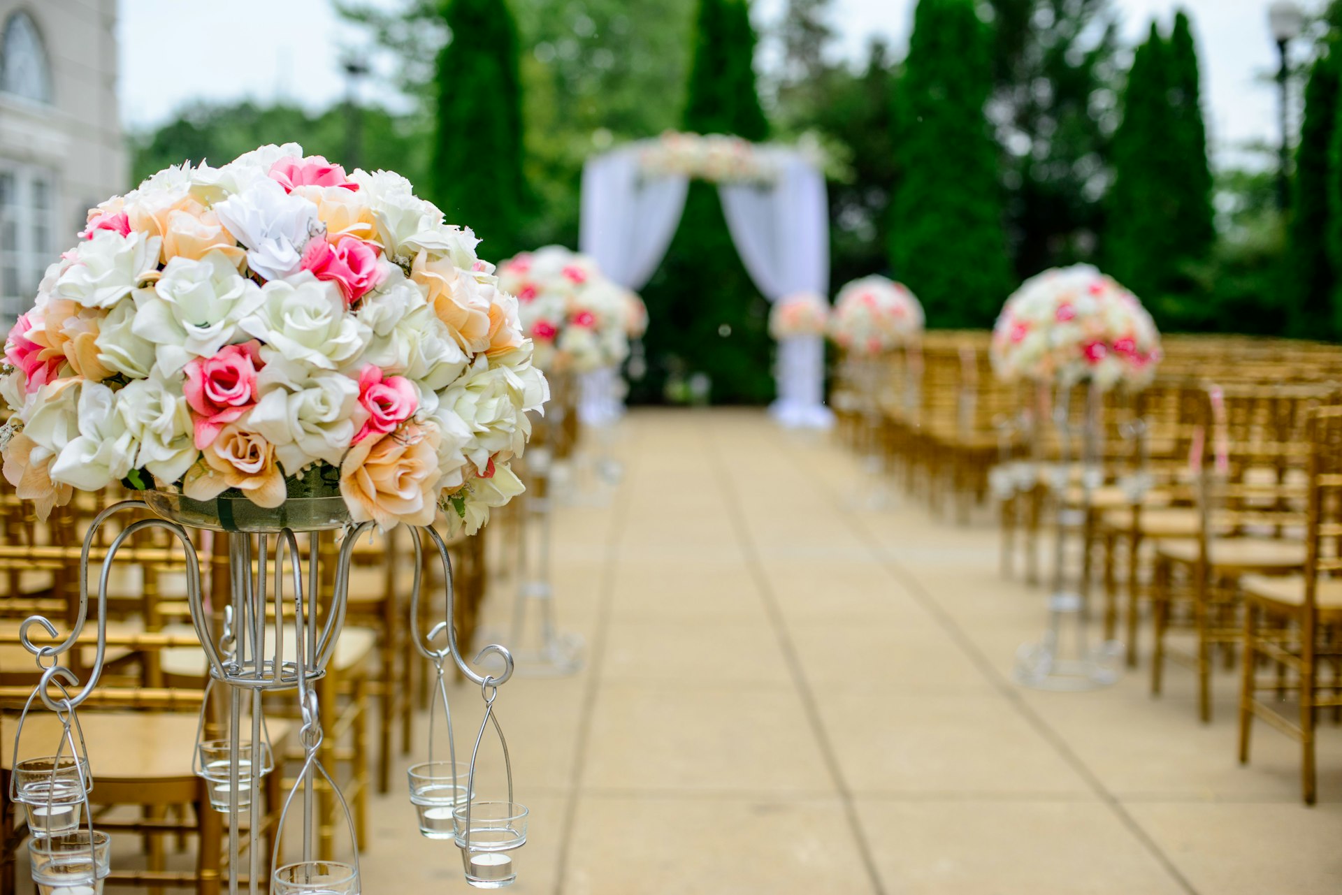 Luxury event styling — outdoor floral aisle with gold chairs